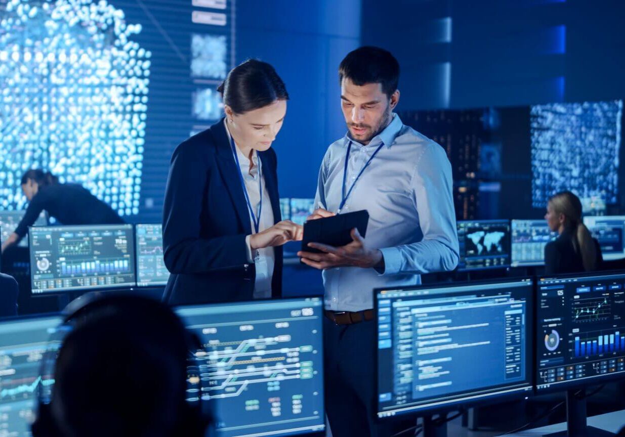 Project Manager and Computer Science Engineer Talking while Using A Digital Tablet Computer. Telecommunications Company System Control and Monitoring Office Room with Working Specialists.