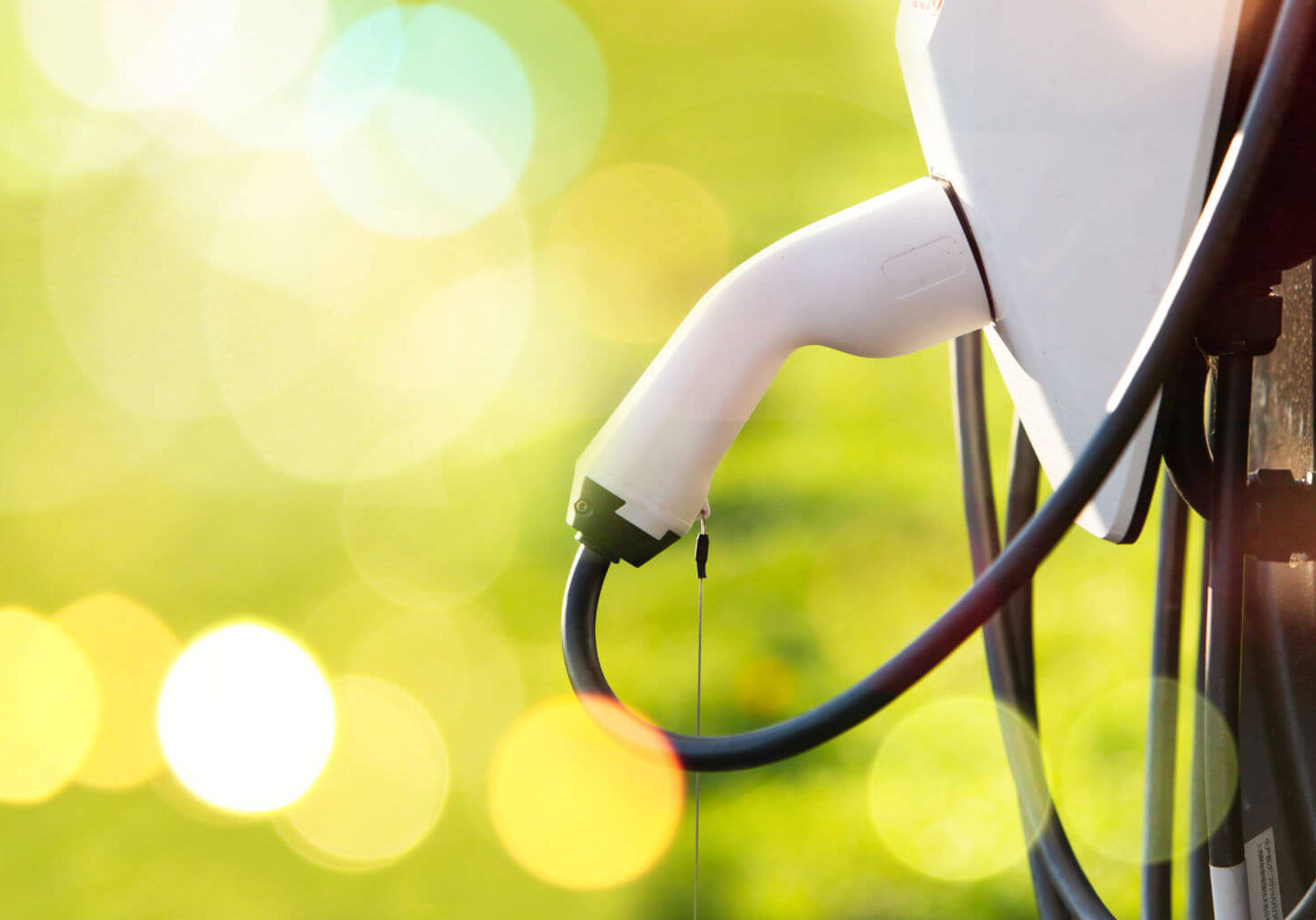 Power supply for electric car charging. Electric car charging station. Close up of the power supply plugged. Green grass blur background