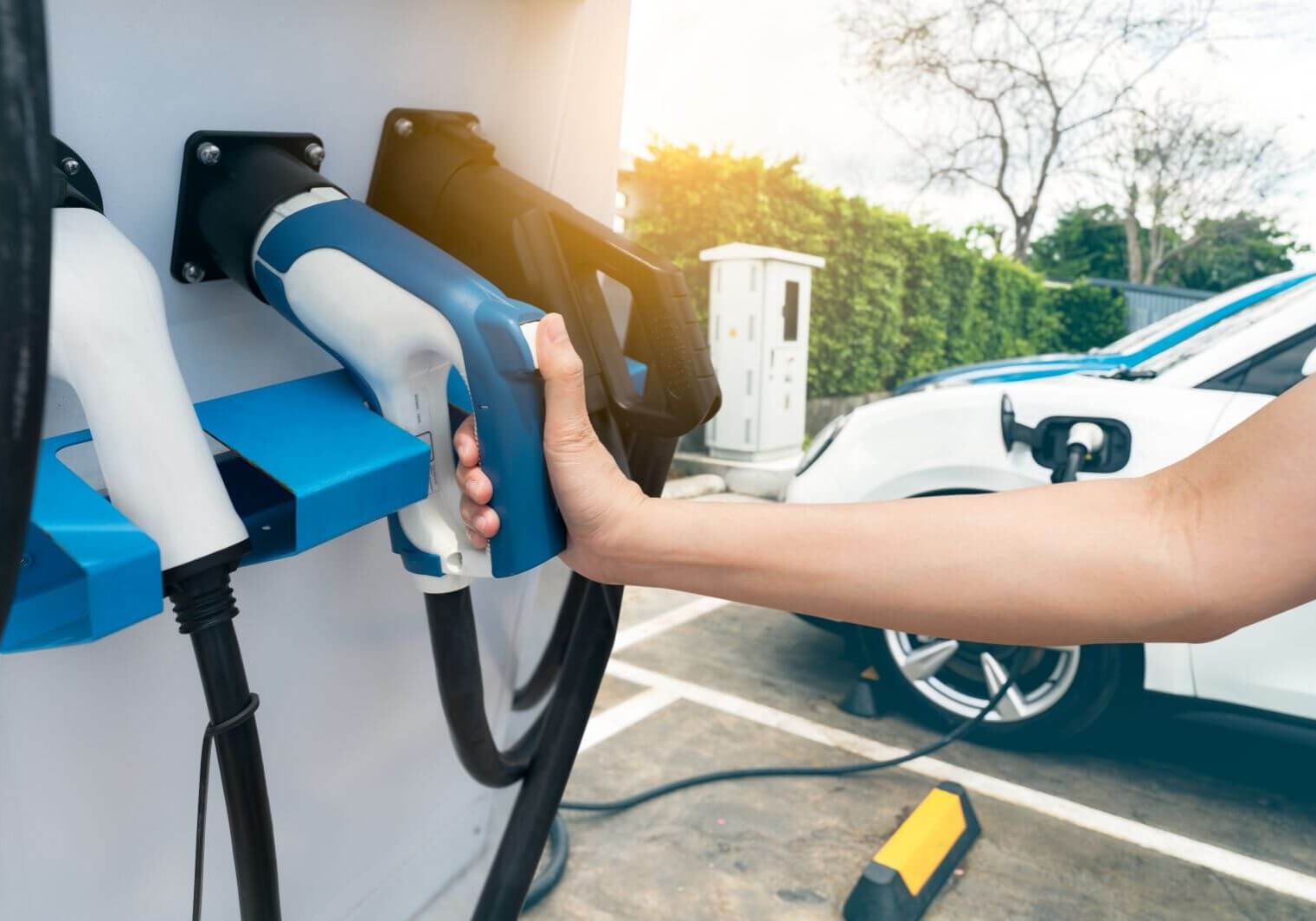 Hand holding electric plug-in charger on blur car charging. EV car charging at electric car charging station. EV car charging point. Electric vehicle fast charge. Sustainable power. Green energy.