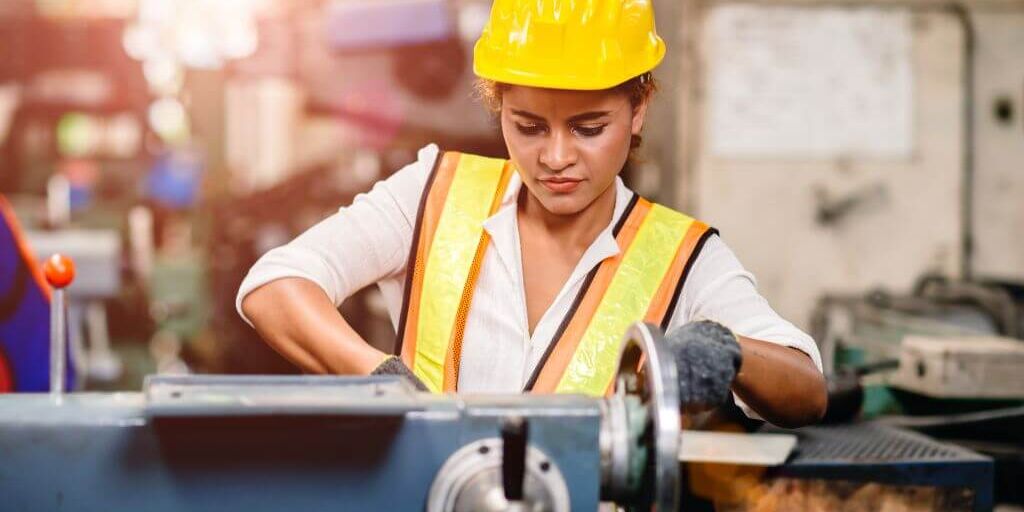 Girl teen worker african american working labor in industry factory with heavy steel machine.