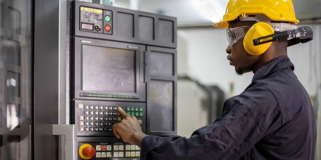 Portrait of African American mechanic engineer worker wearing safety equipment beside the automatic lathe machine in manufacturing factory